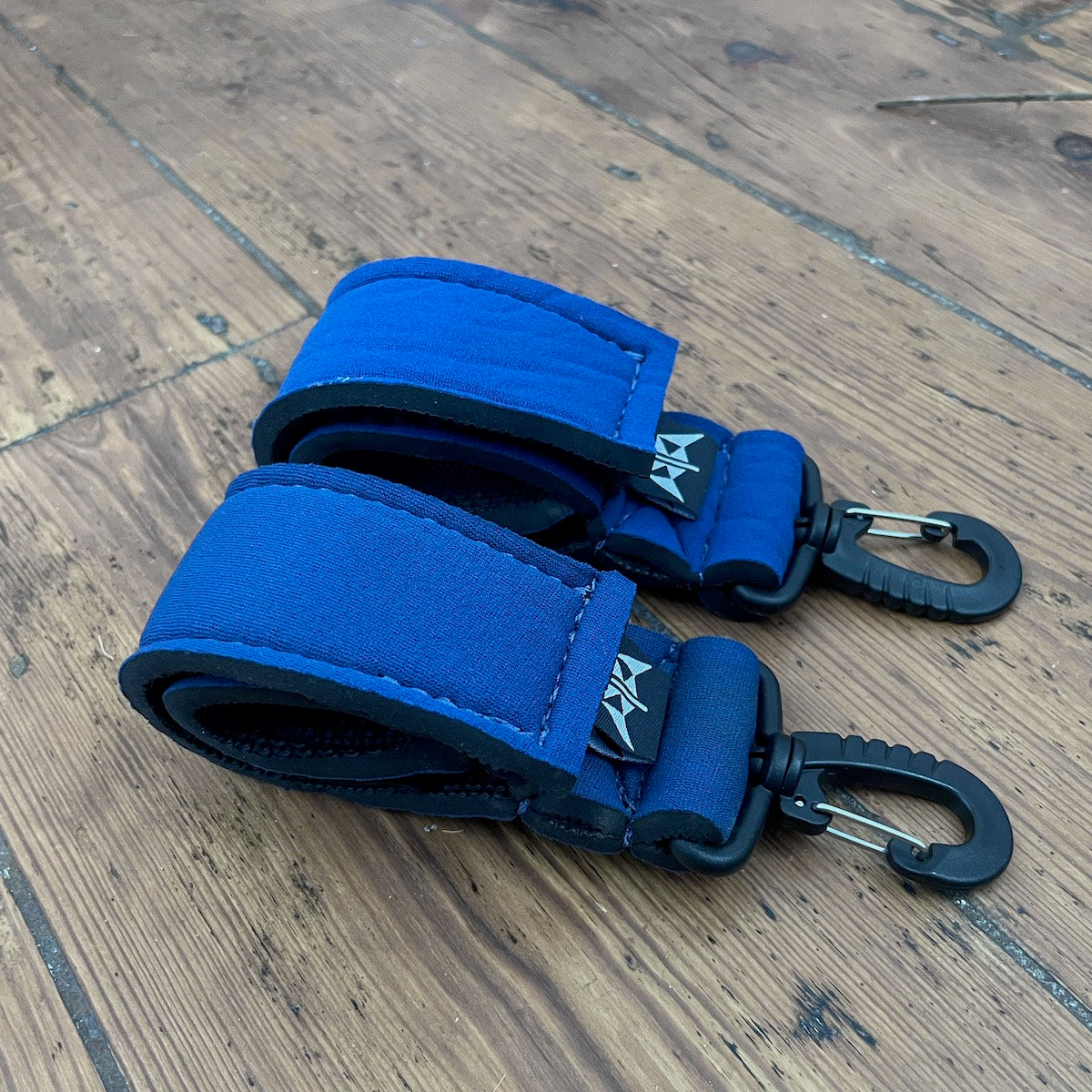 A pair of blue and black velcro paddle keepers with clips, placed on a wooden surface.