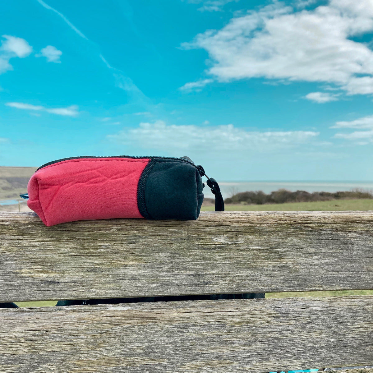 Red and black pouch on a wooden surface with a blue sky and clouds in the background