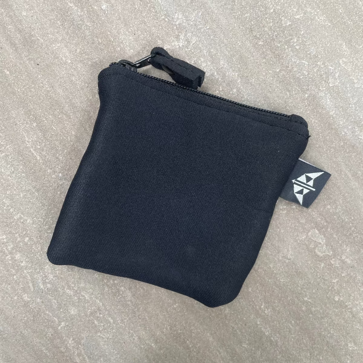 Black zippered pouch with a brand tag on a gray surface