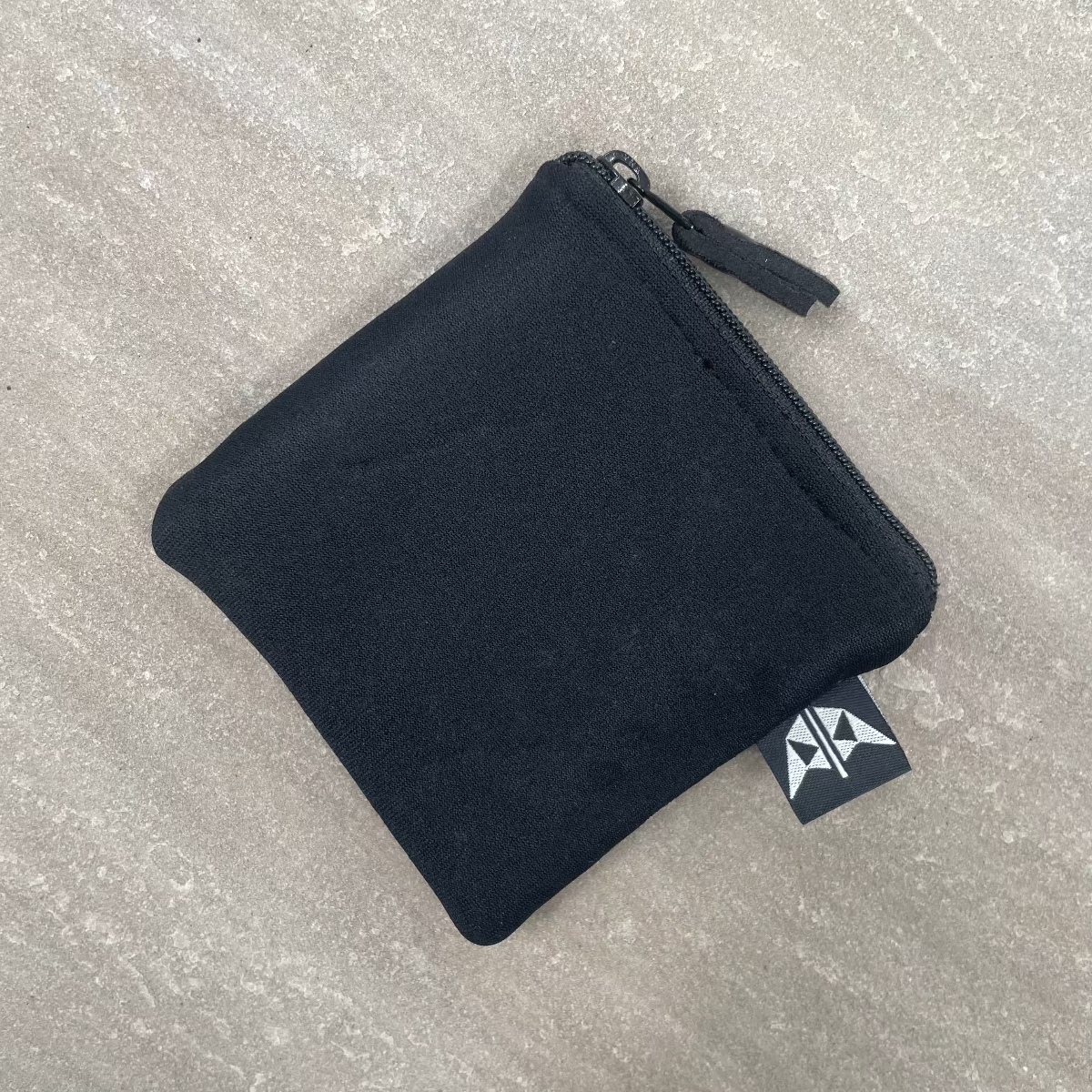 Black zippered pouch on a gray textured surface with a visible brand tag.