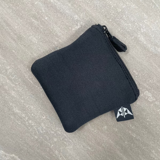 Black zippered pouch on a gray textured surface with a brand logo.