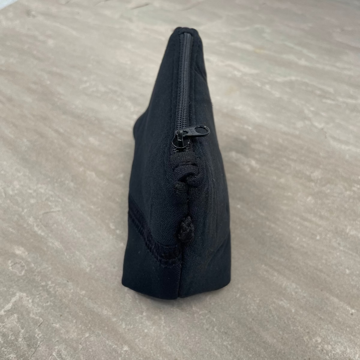 Black triangular pouch with a zipper on a gray surface