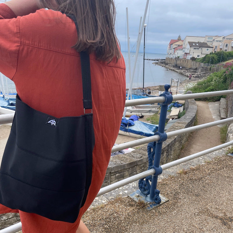 Recycled tote bag made from black recycled wetsuits worn in a marine setting.