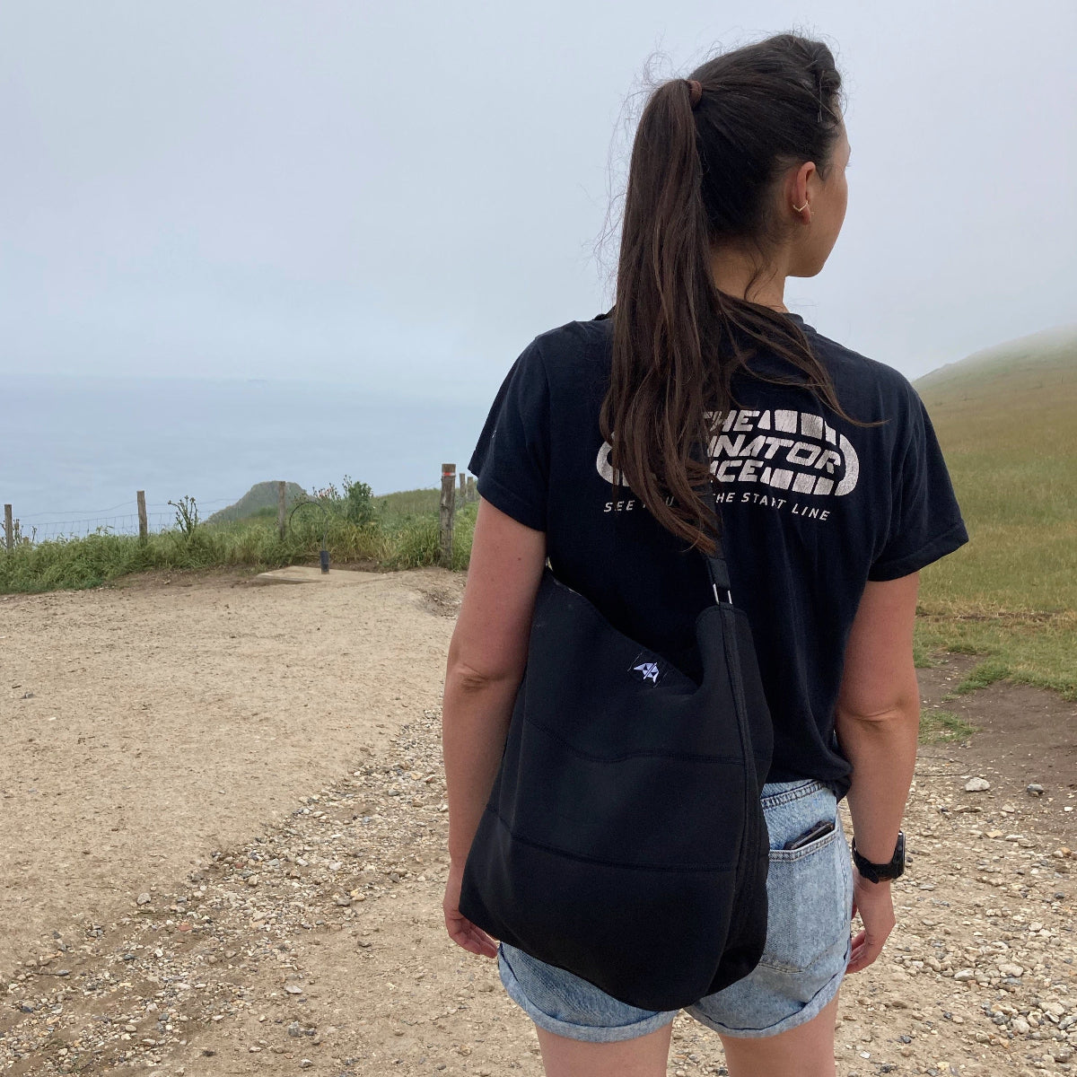 Everyday tote bag made from black recycled wetsuits worn in a sea, cliffside setting.